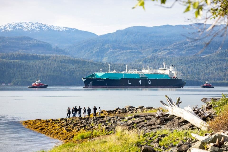 An LNG carrier docked at a terminal, with industrial infrastructure in the background.